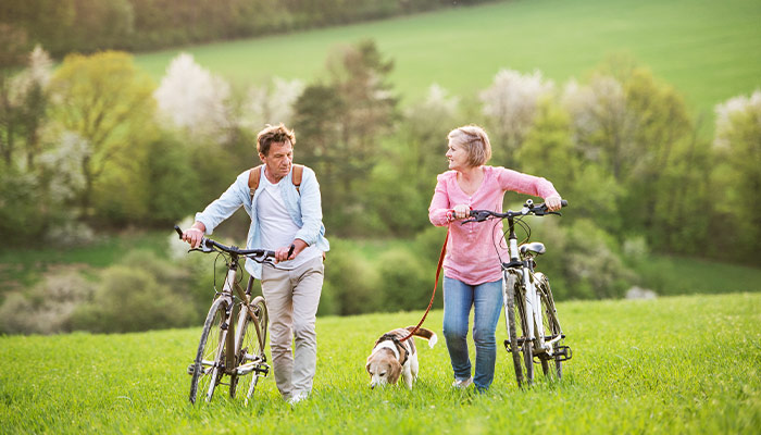 couple pushing their bikes in a field with their dog at their side life insurance in retirement